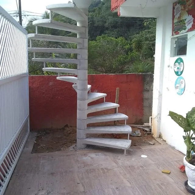 Escada caracol real em execução, com coluna central de concreto e degraus aparentes em uma área externa